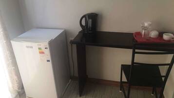 Una kitchenette compacta con refrigerador, cafetera, una mesita con una silla y una bandeja roja.