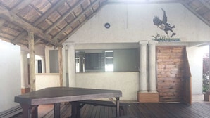A covered outdoor area with a wooden table and benches, a brick wall, and a mural of an eagle. - Eagle Suites Guest House (Ghanzi)