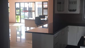 A kitchen with white cabinets, a countertop, and a view of a dining area with a table and chairs. - Eagle Suites Guest House (Ghanzi)