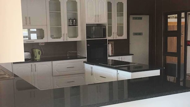 A modern kitchen with white cabinetry, a black countertop, and a microwave. - Eagle Suites Guest House (Ghanzi)