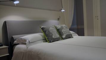 Una cama bien hecha con ropa de cama blanca y dos almohadas con estampado de pájaros. Hay una lámpara de noche en la mesita.