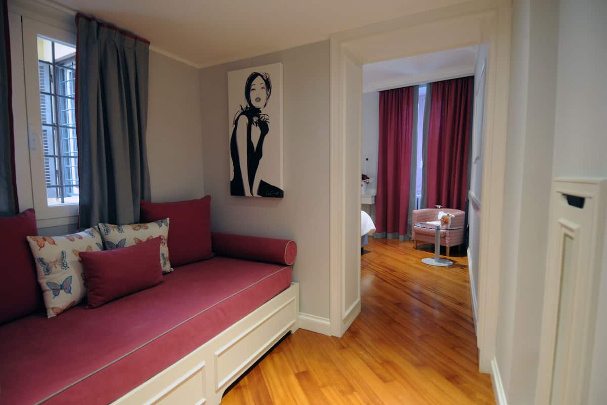 A room with a red sofa, a wall-mounted artwork, and a view through an open door to another room with a red curtain.