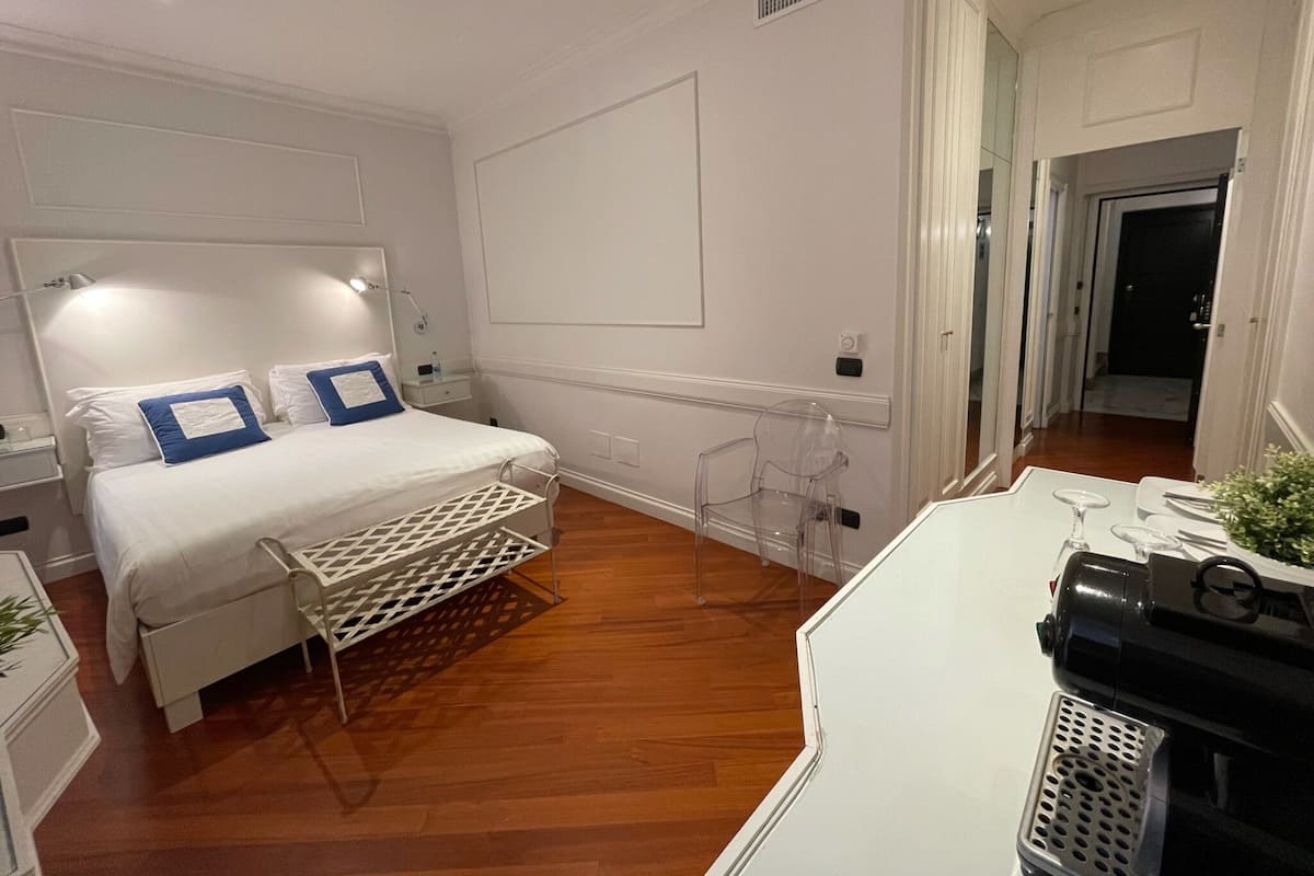 A hotel room with a bed, bedside tables, a desk with a chair, and a small plant.