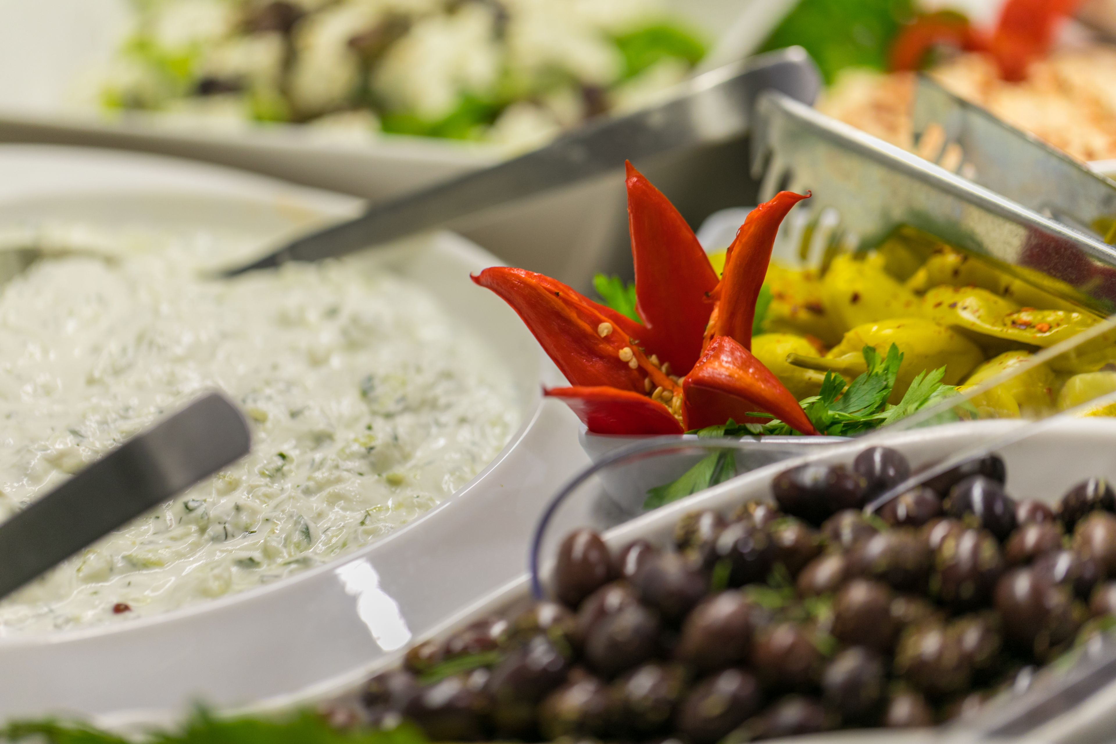 Een buffet met diverse gerechten, waaronder een witte, romige dip, een schotel met rode chilipepers en een kom olijven.