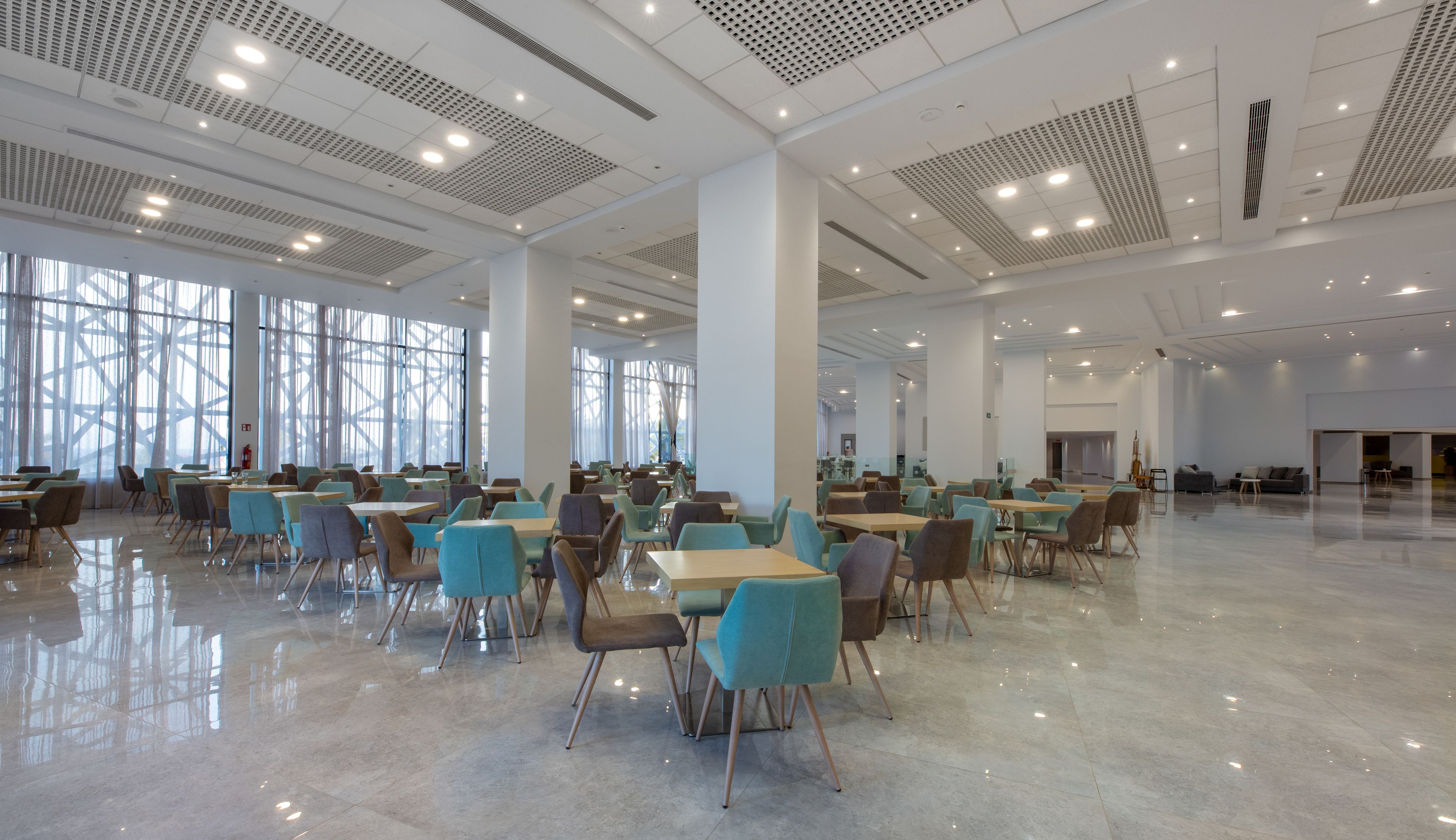 Un espacio interior amplio con mesas y sillas dispuestas para comer, grandes ventanales que dejan entrar luz natural, y un diseño de techo moderno.