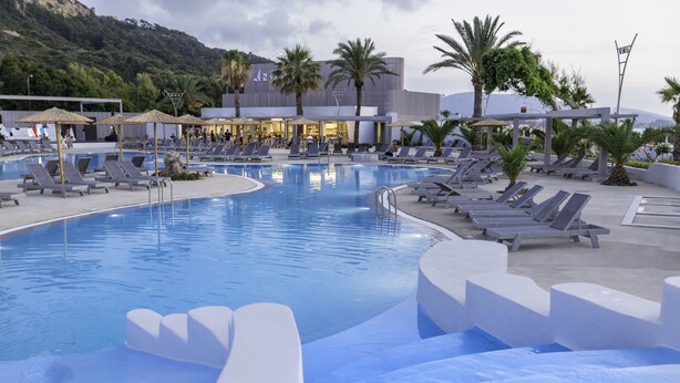 A pool area with multiple sun loungers and umbrellas, surrounded by palm trees and a building with a modern design. - Akti Imperial Deluxe Resort & Spa Dolce by Wyndham - All inclusive (Rhodes)
