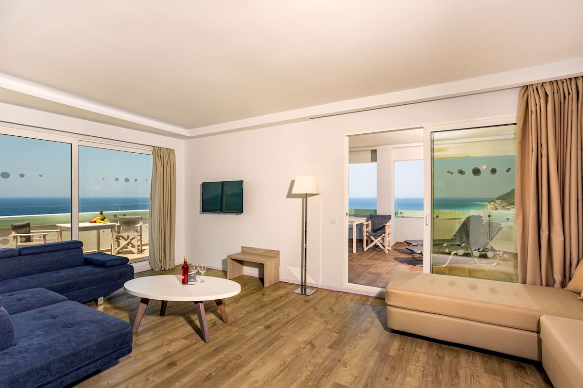 Une chambre d’hôtel moderne dotée d’un grand balcon, d’un canapé, d’une table ronde et d’un téléviseur.