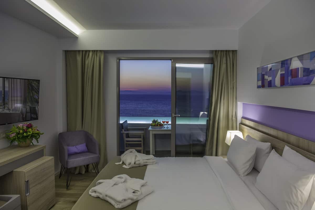 Ein Hotelzimmer mit Bett, Schreibtisch, Stuhl, Fernseher und einem Balkon mit Meerblick.