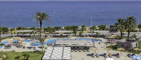 Un complex turístic amb zona de piscina, gandules, ombrelles i vista al mar.