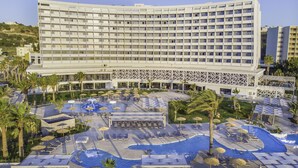 A modern hotel with a large pool area, multiple lounge areas, and a prominent building facade.