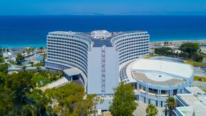 A modern hotel with a curved facade, a central atrium, and a pool area. - Akti Imperial Deluxe Resort & Spa Dolce by Wyndham - All inclusive (Rhodes)