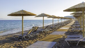 A beach with rows of sun loungers and thatched umbrellas along the shoreline. - Akti Imperial Deluxe Resort & Spa Dolce by Wyndham - All inclusive (Rhodes)