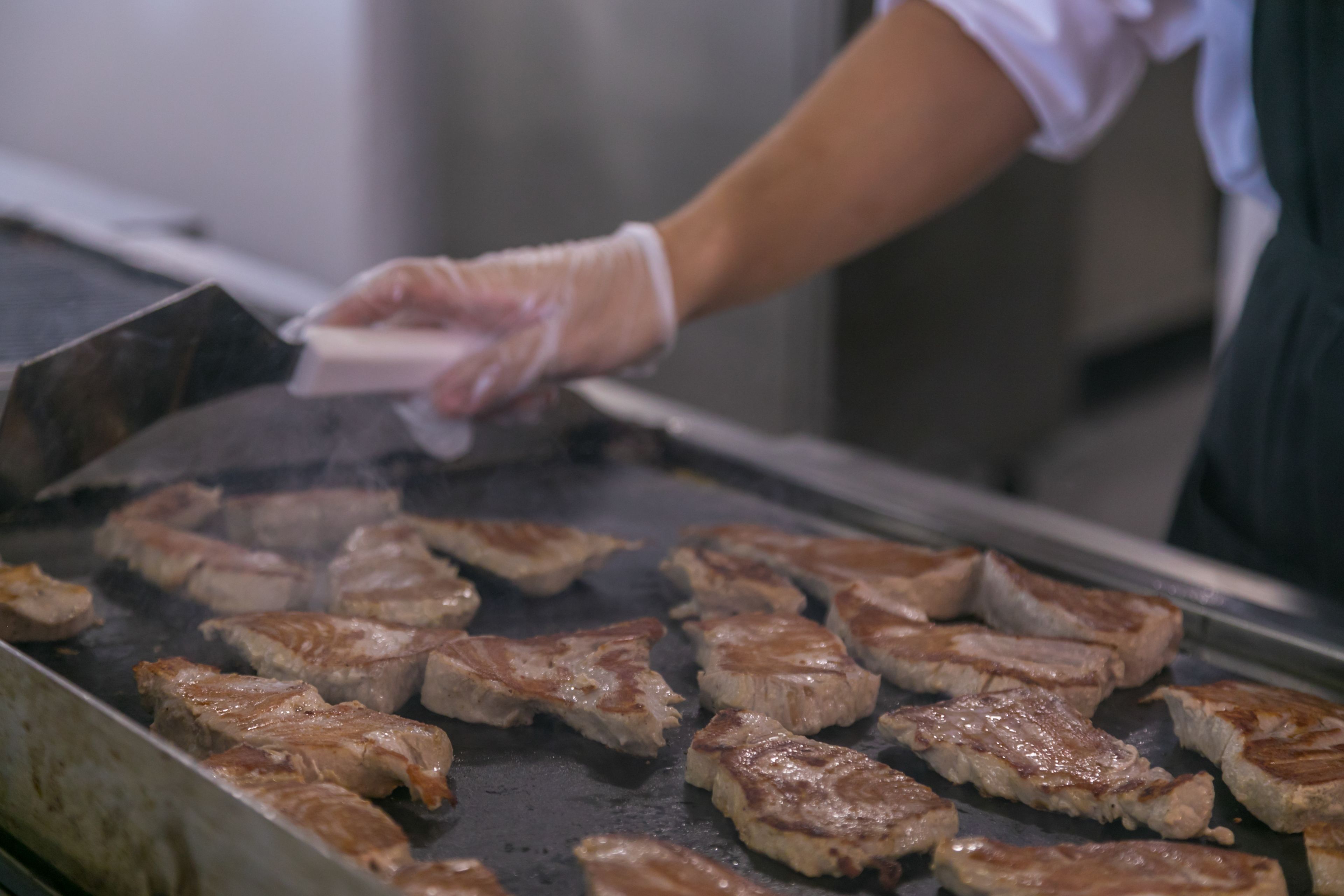 A person cooking meat on a grill in a kitchen.