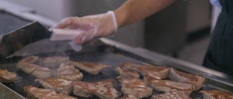 Una persona cocinando carne en una parrilla dentro de una cocina.