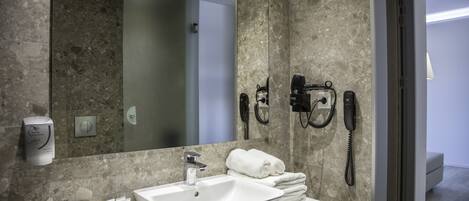 Un baño moderno con un espejo grande, un lavamanos y un perchero para toallas. Hay artículos de aseo en la encimera y un teléfono montado en la pared.