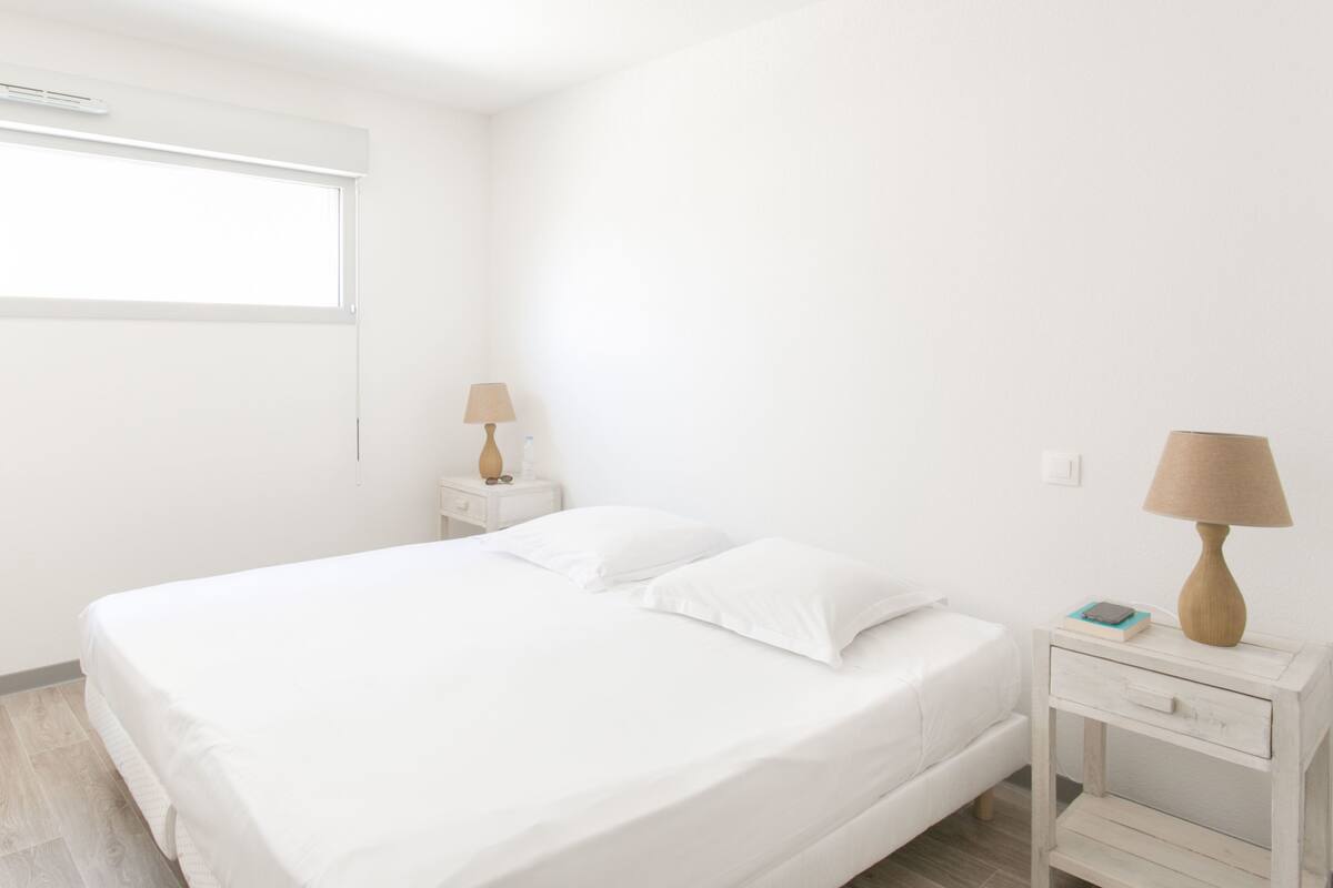 Un dormitorio minimalista con una cama individual, dos mesitas de noche y un ventanal.