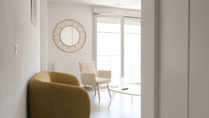 Un salon moderne comprenant un canapé, deux fauteuils, une table basse et une grande fenêtre équipée de stores.