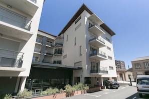 Un edificio residencial de varios pisos con balcones, una zona de estacionamiento techada y un cielo azul despejado.