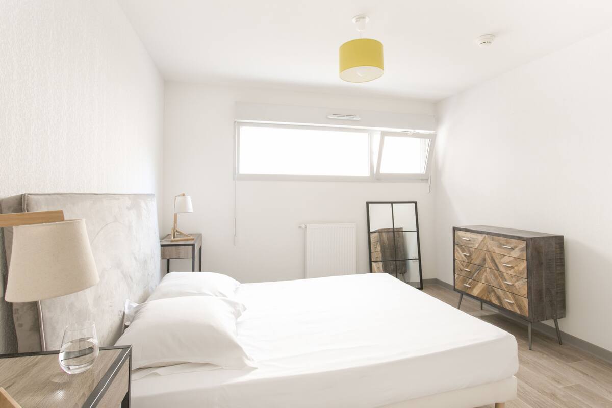 Un dormitorio moderno con cama, mesita de noche, lámpara y cómoda.