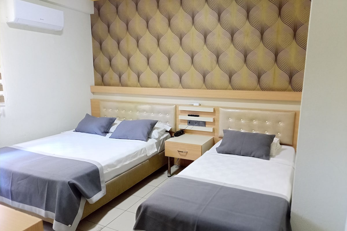 A hotel room with two single beds, a bedside table with a phone, and a wall-mounted air conditioner.