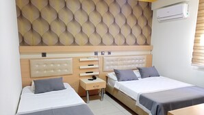 Een hotelkamer met twee bedden, een nachtkastje met een telefoon en koptelefoon, een wandairconditioner en behang met een patroon.