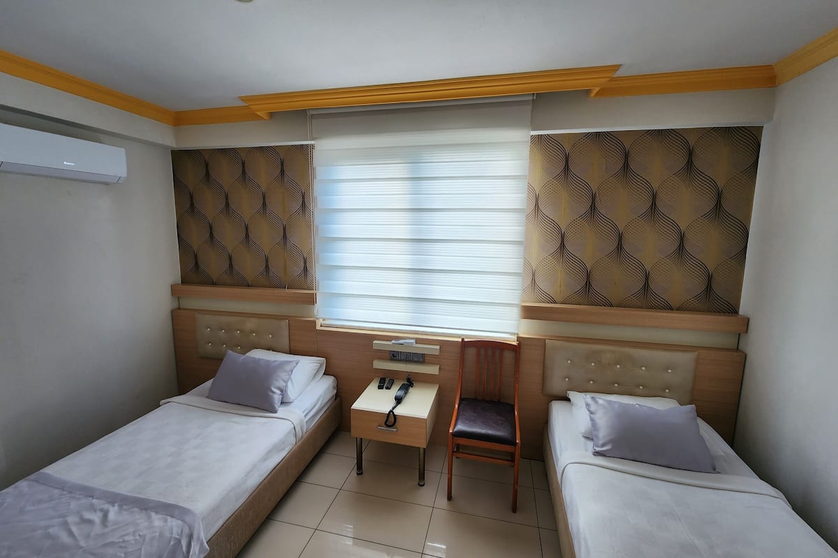 A room with two single beds, a desk with a chair, and a window with blinds.