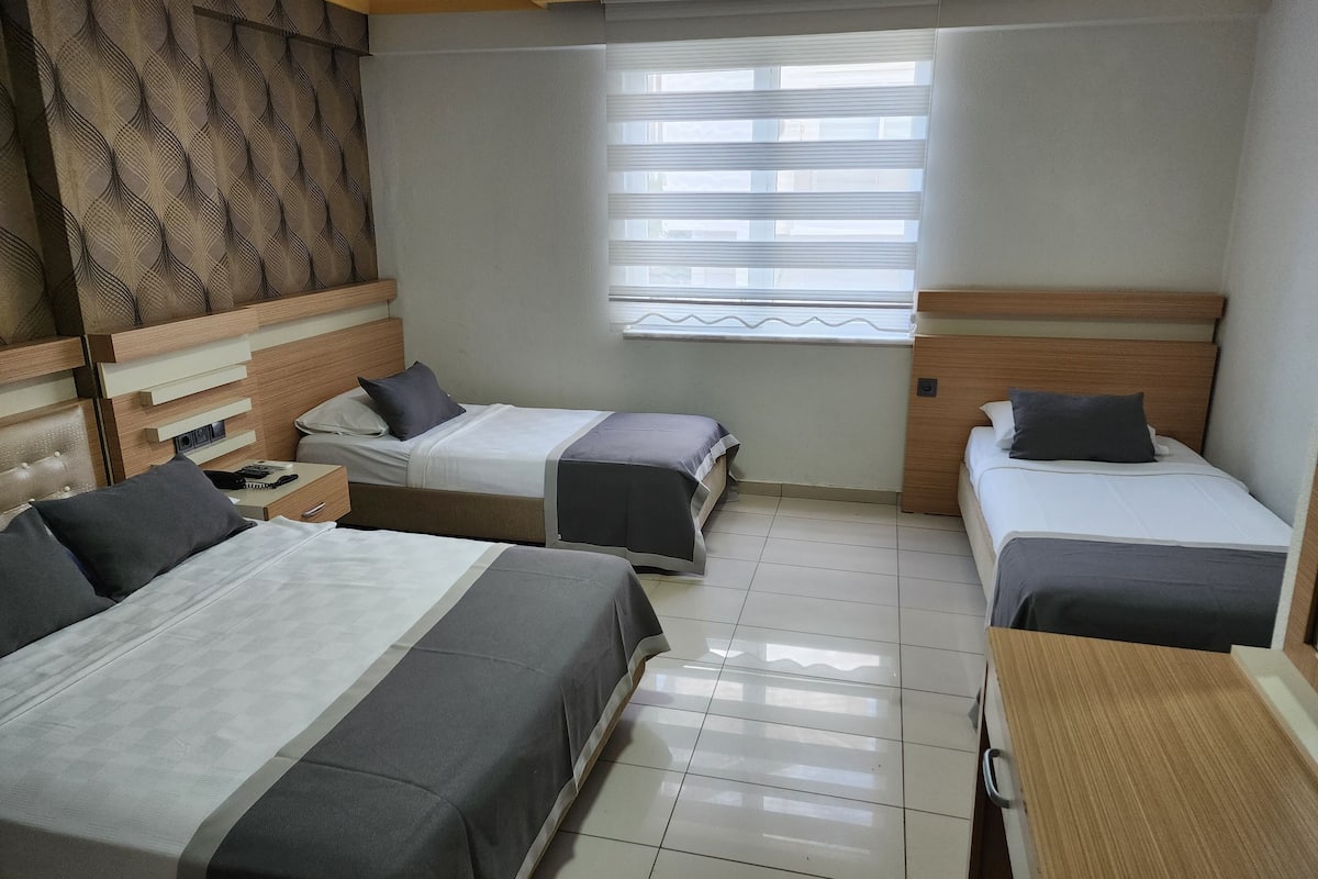 A hotel room with two single beds, a wooden headboard, a small table, and a window with blinds.