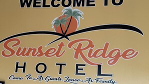 Une enseigne fixée au mur de l’hôtel Sunset Ridge, portant les inscriptions suivantes : « BIENVENUE À L’HÔTEL SUNSET RIDGE » et « Entrez en tant qu’invités, repartez en tant que membres de la famille. »