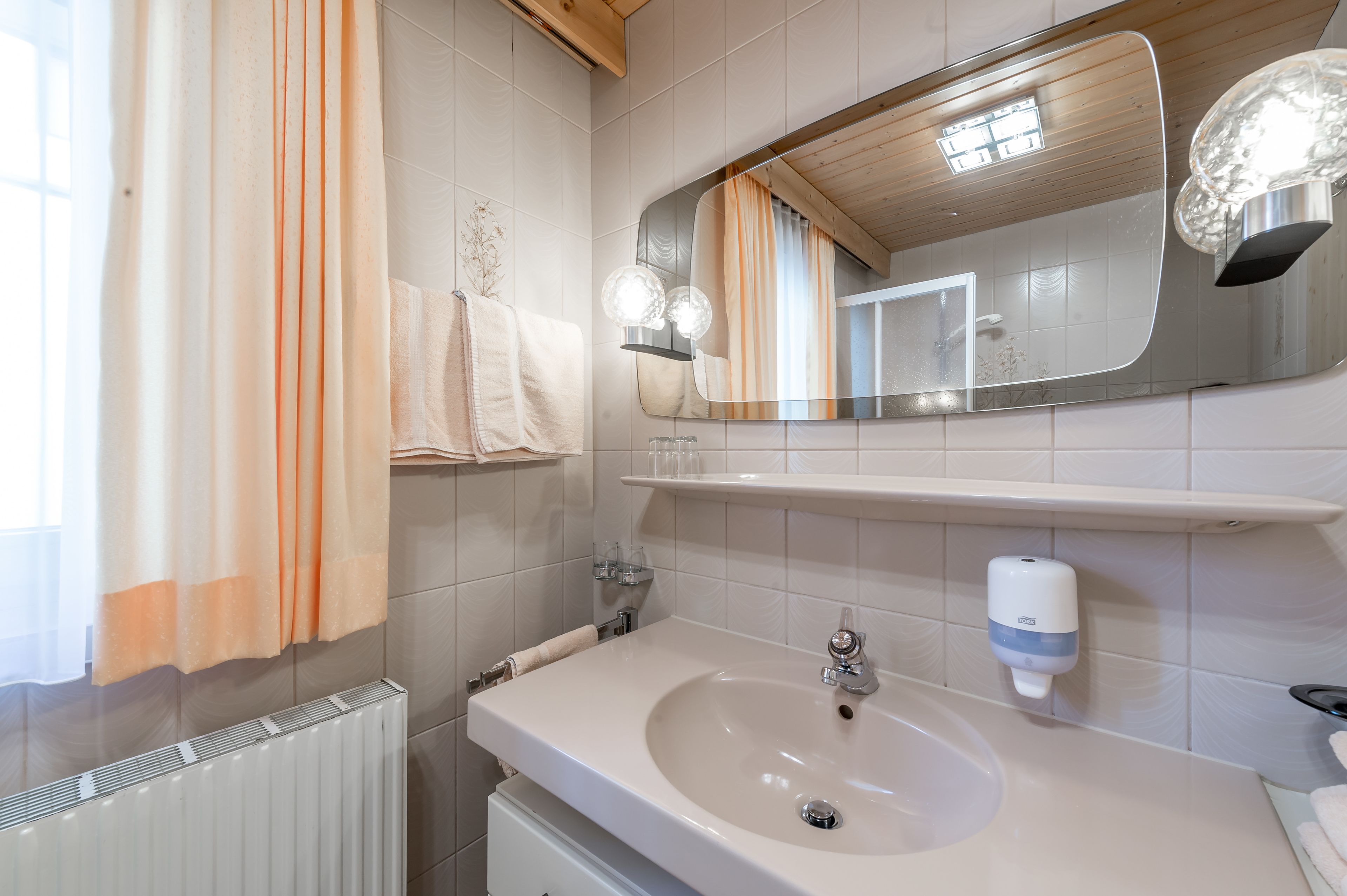 A bathroom with a white sink, a mirror, a towel rack, and a towel dispenser.
