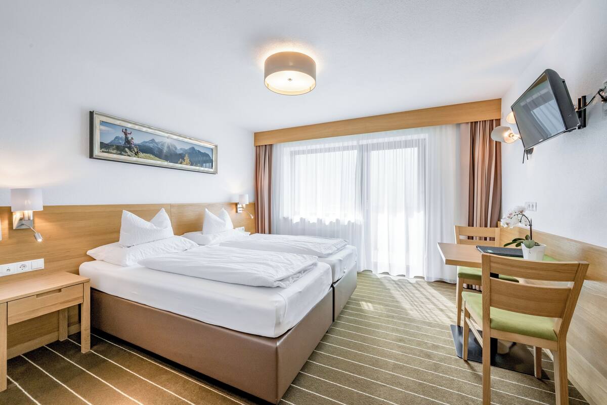 A hotel room with two beds, a desk, a chair, a television, and a window with curtains.