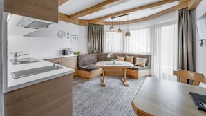 A modern kitchen with a built-in oven, a sink, and a countertop. There is a dining area with a table and chairs. The room has wooden beams on the ceiling and large windows with curtains. - Apart Hotel Garni Wieser - Sölden (Soelden)