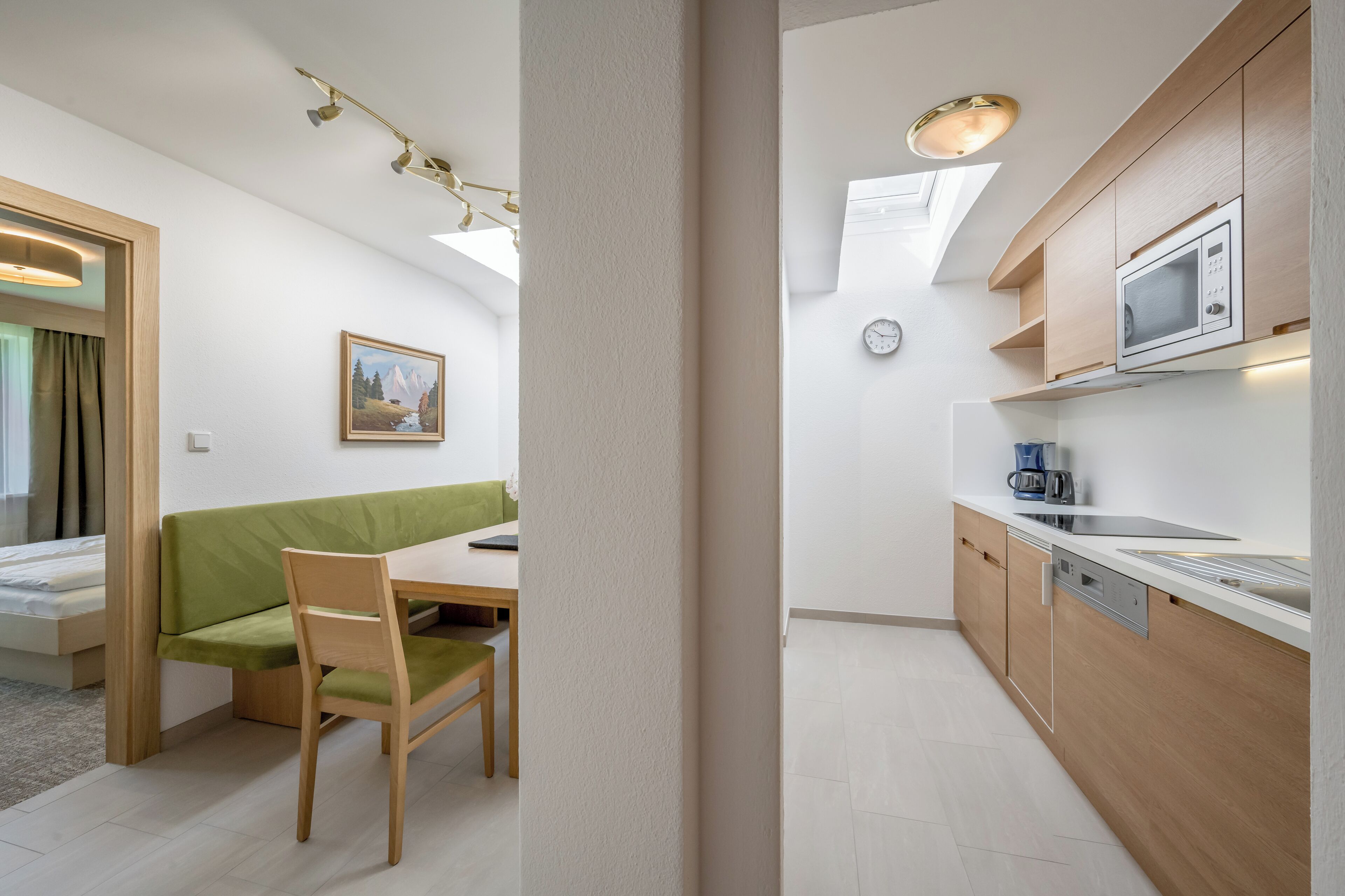 Ein kleines Zimmer mit einem grünen Sofa, einem Holzespeisetisch und einer Küchenzeile inklusive Mikrowelle und Kaffeemaschine.