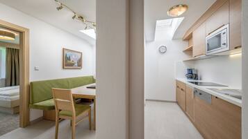 Ein kleines Zimmer mit einem grünen Sofa, einem Holzespeisetisch und einer Küchenzeile inklusive Mikrowelle und Kaffeemaschine.