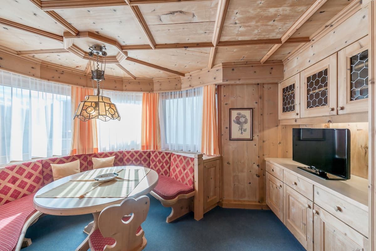 A cozy cabin interior with a round dining table, a bench with a checkered cushion, a television on a wooden cabinet, and a ceiling fan.