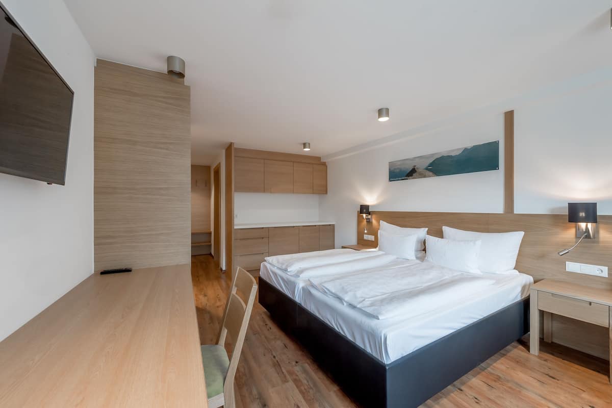 A modern hotel room with a large bed, wooden flooring, a flat-screen TV, and a painting on the wall.