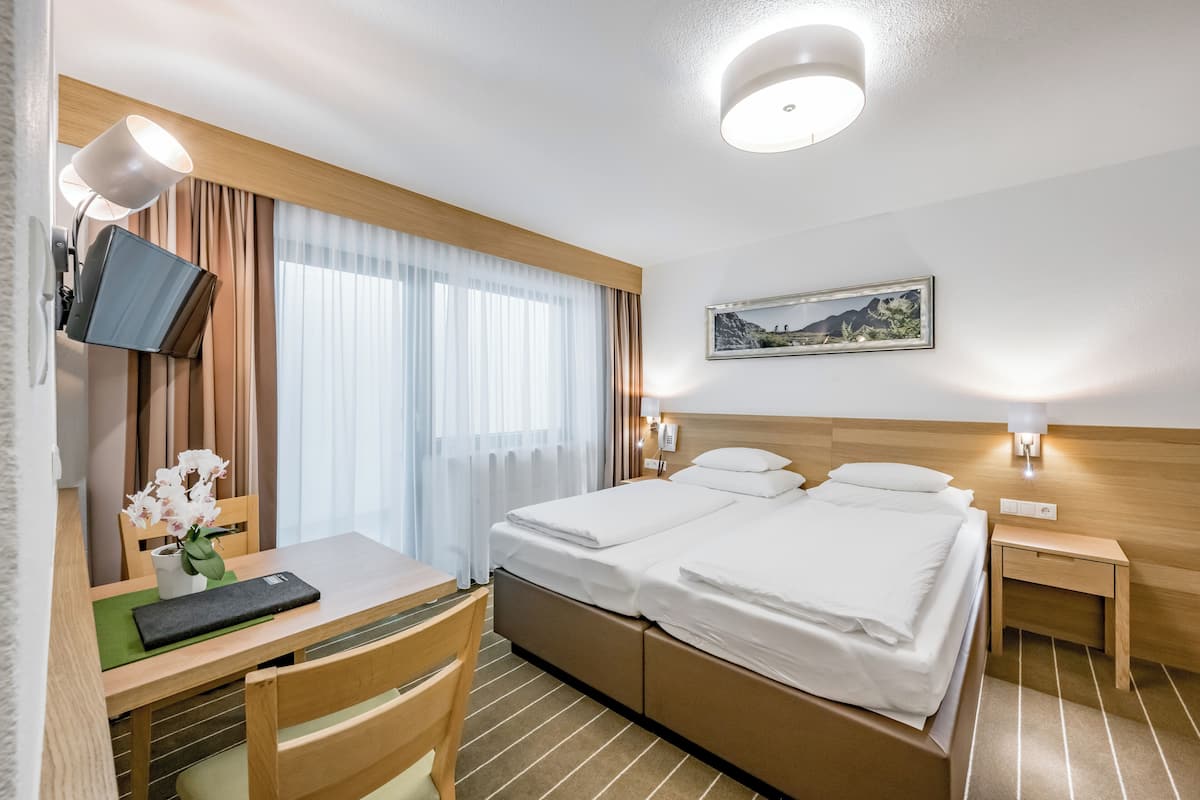 A hotel room with a bed, a desk, a chair, a TV, and a painting on the wall.