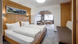 A hotel room with a large bed, a wooden headboard, a framed picture, and a view into the dining area. - Apart Hotel Garni Wieser - Sölden (Soelden)
