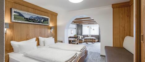 A hotel room with a large bed, a wooden headboard, a framed picture, and a view into the dining area.