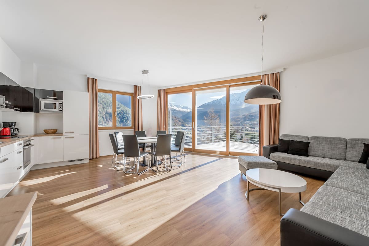 A modern apartment with a kitchen, dining area, and living room with a large window offering a mountain view.