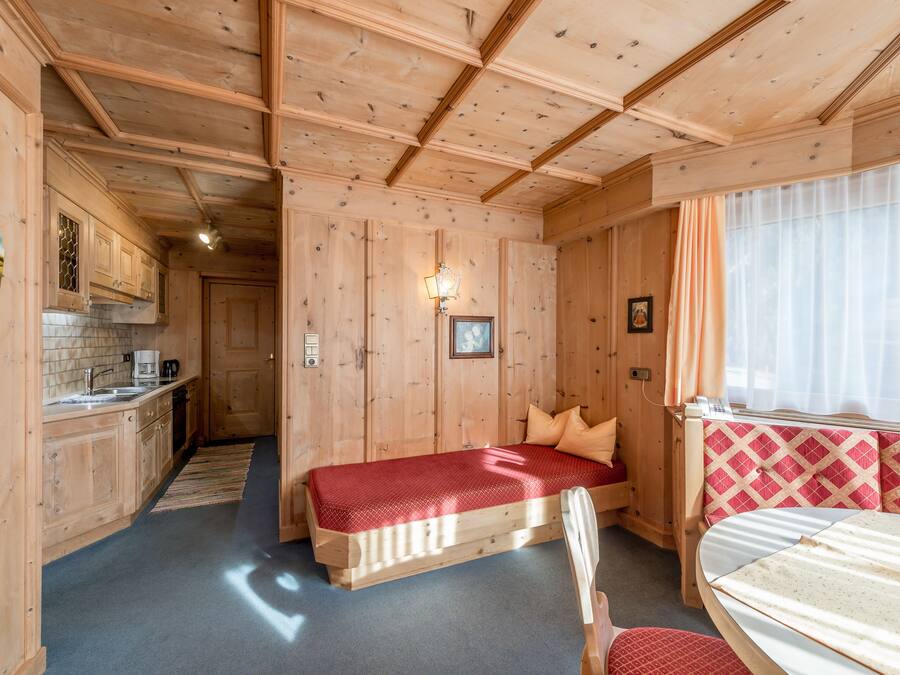 Interior de una cabaña de madera con cama, una kitchenette pequeña y una ventana con cortinas.