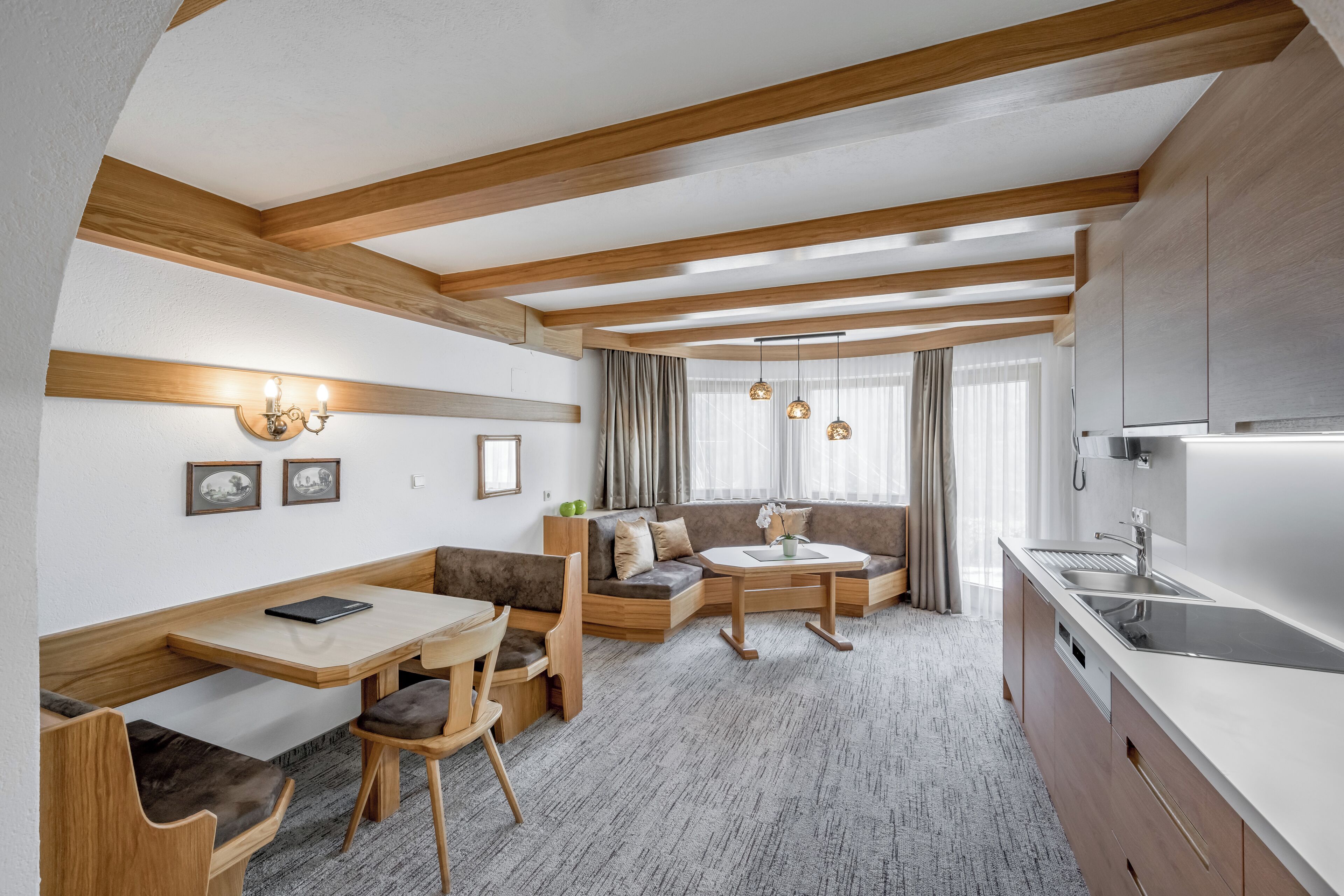 Eine moderne Küche mit Holzbalken, einem Essbereich mit einer Bank und einer Sitzecke mit Sofa und Tisch.