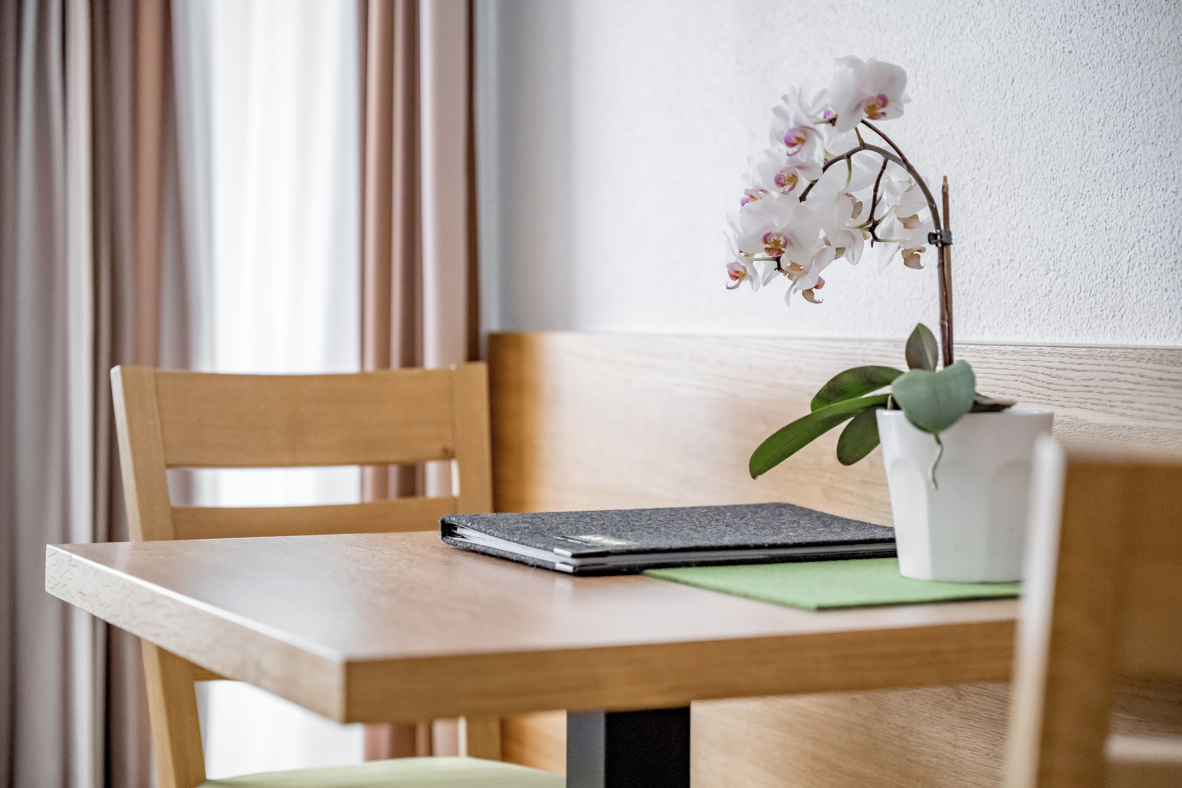 A wooden table with a laptop, a notebook, and a potted orchid.