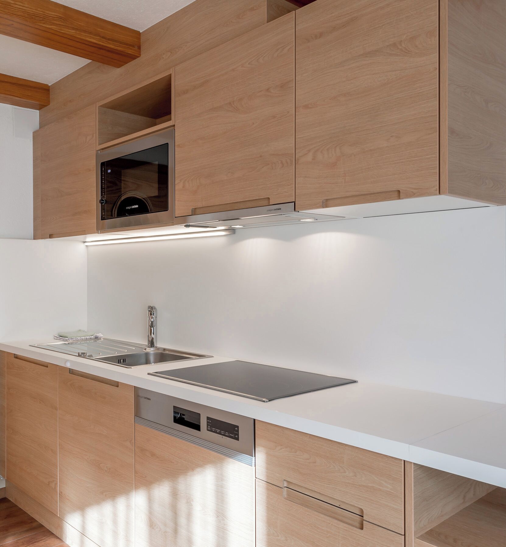 A modern kitchen with wooden cabinets, a built-in oven, and a stainless steel sink.