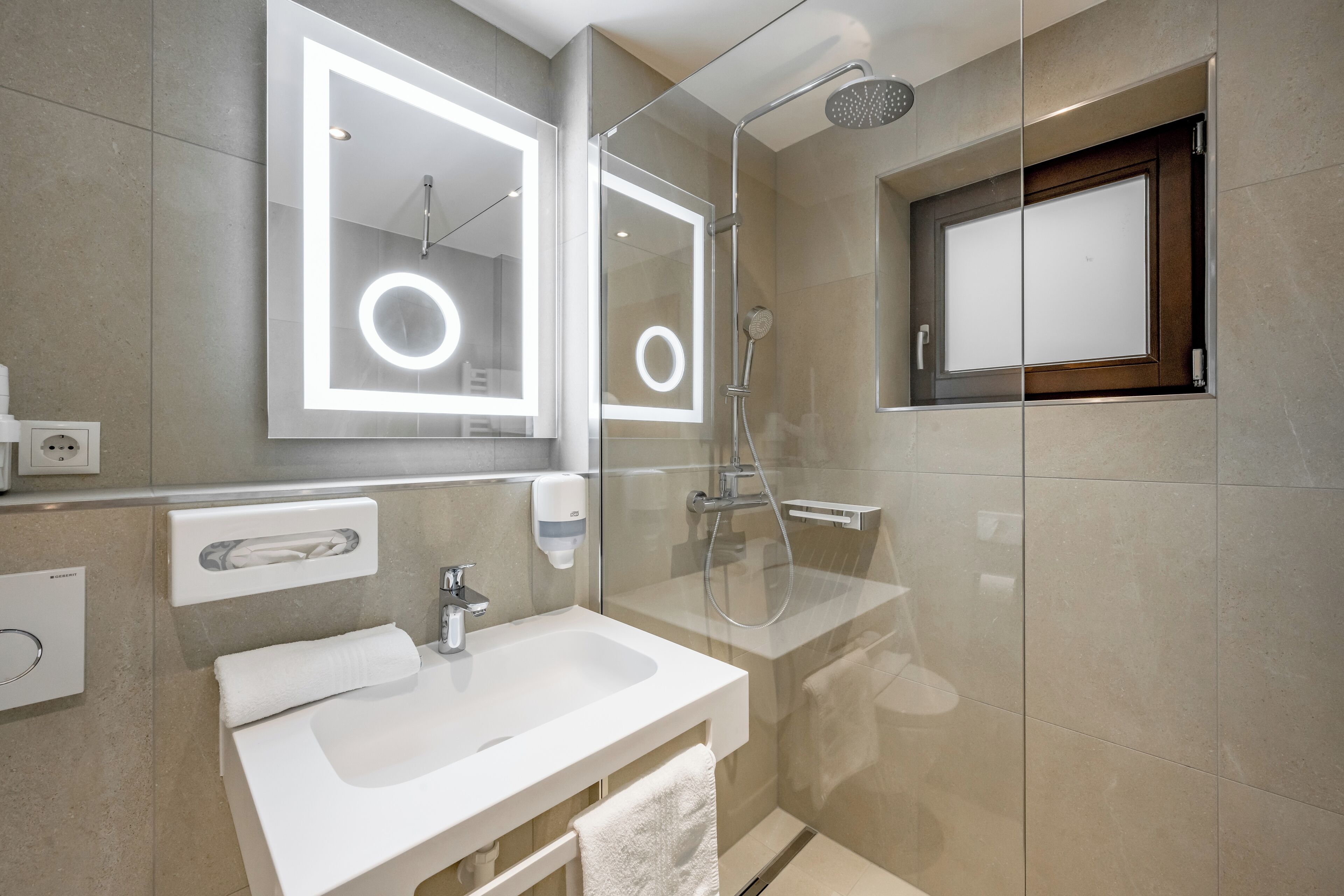 A modern bathroom with a large mirror, a sink, a shower, and a window.