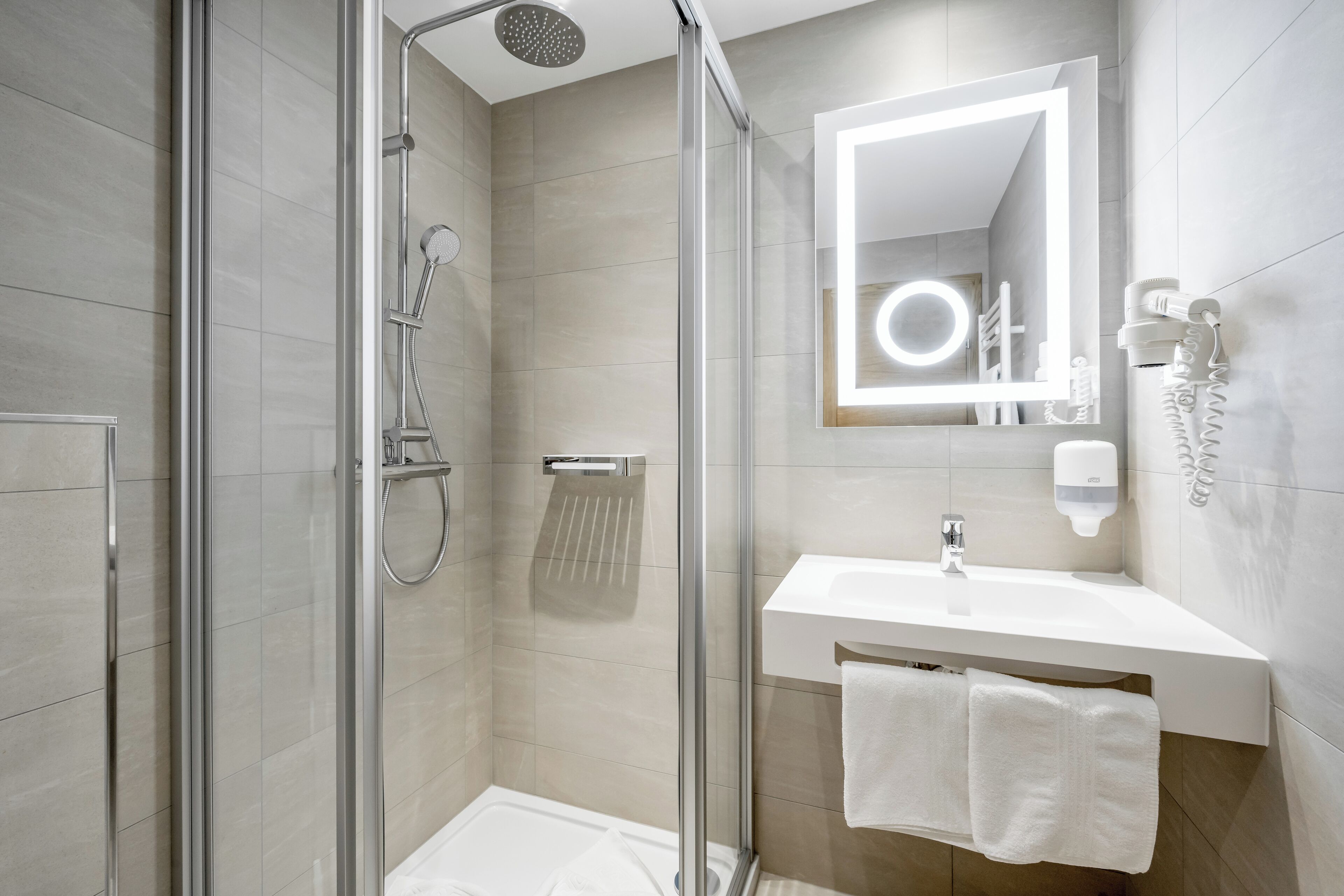 A modern bathroom with a glass-enclosed shower, a white sink, and a mirror with built-in lighting.