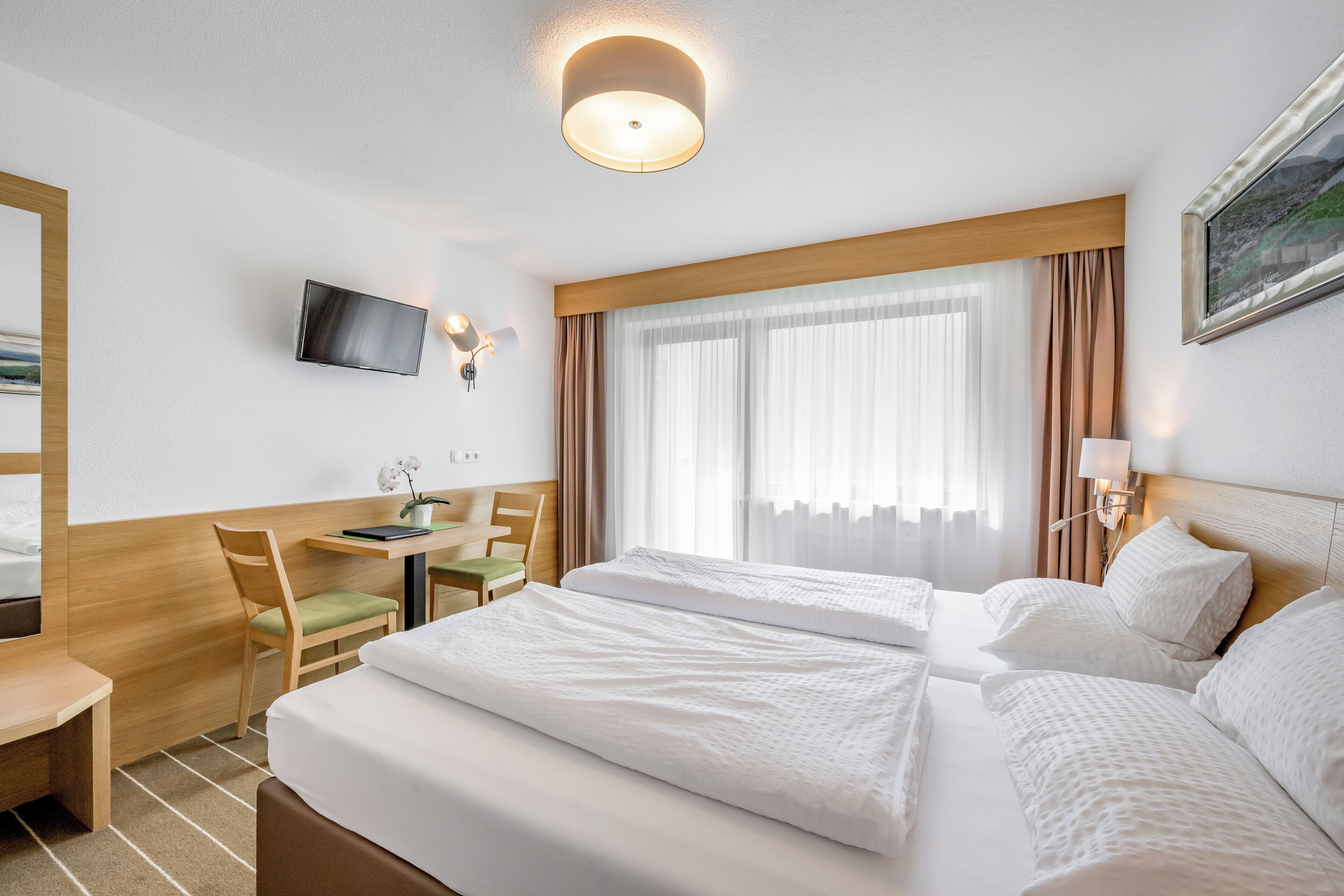 Ein Hotelzimmer mit Bett, Schreibtisch, Stuhl, Fernseher und einem Fenster mit Vorhängen.