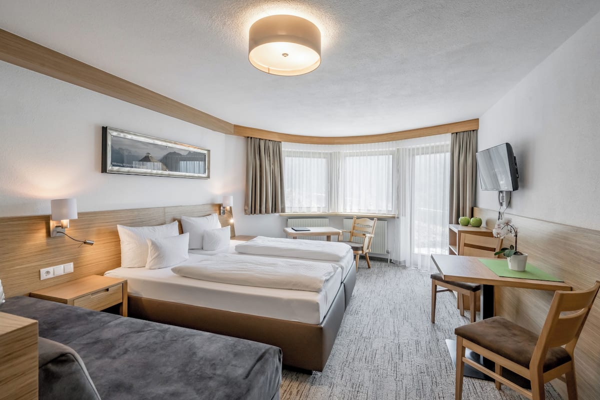 A hotel room with a large bed, a desk, a chair, a TV, and a window with curtains.