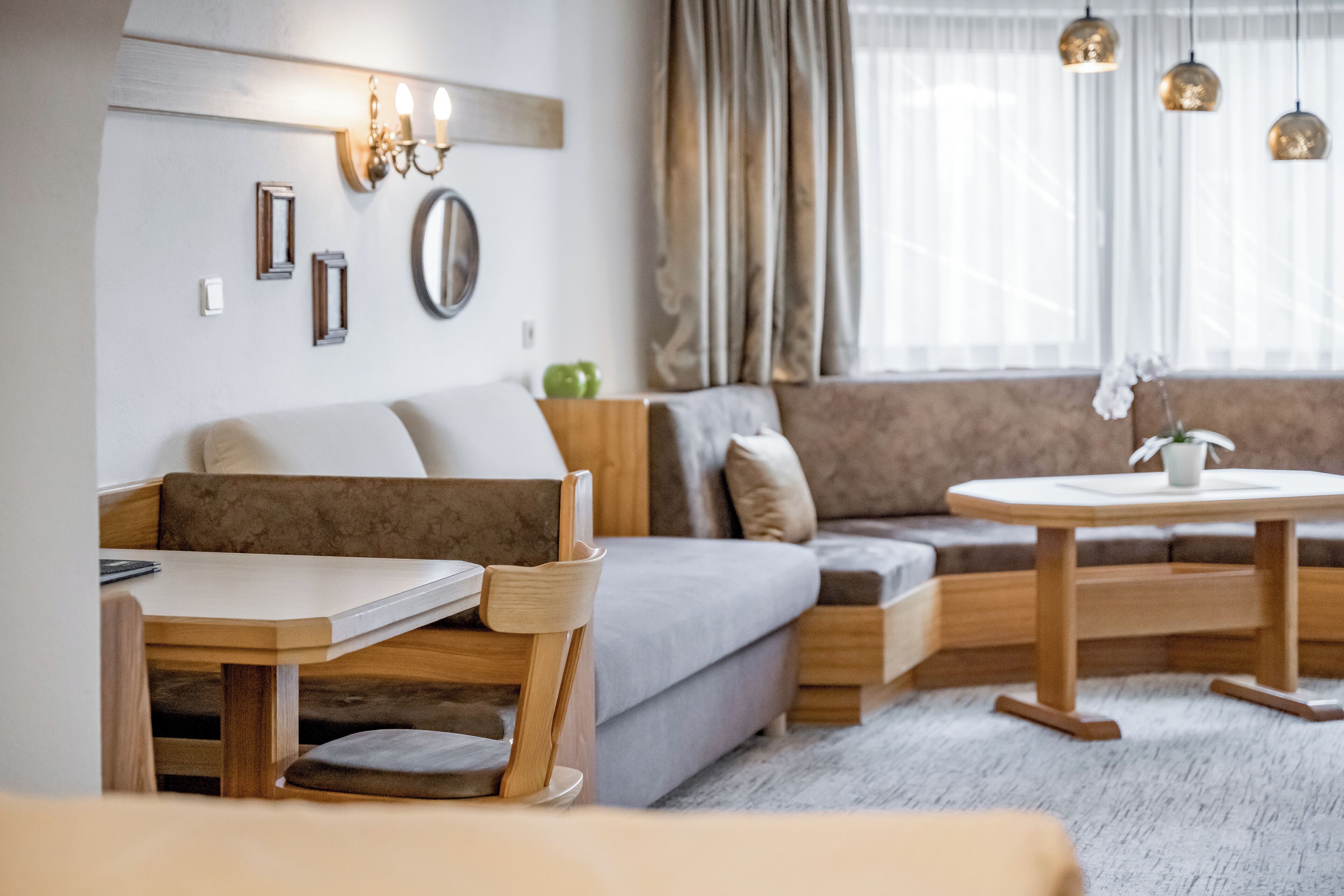 Una sala de estar moderna con un sofá, una mesa de comedor y una mesa de centro. Hay luces fijadas en la pared y una ventana con cortinas.
