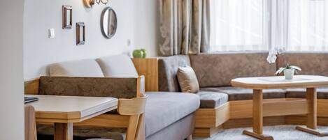Una sala de estar moderna con un sofá, una mesa de comedor y una mesa de centro. Hay luces fijadas en la pared y una ventana con cortinas.