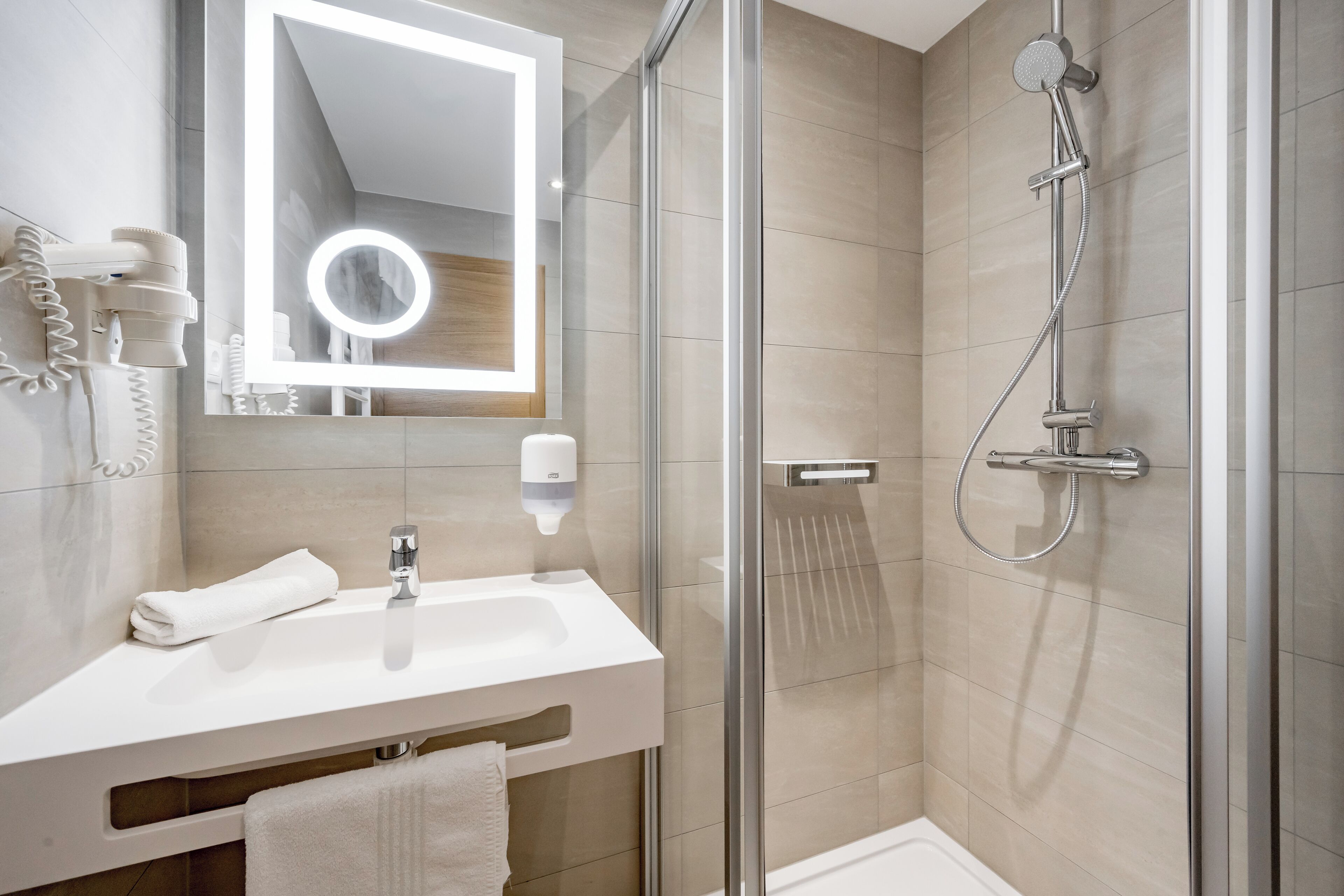 A modern bathroom with a glass-enclosed shower, a white sink, and a mirror with a lighted frame.